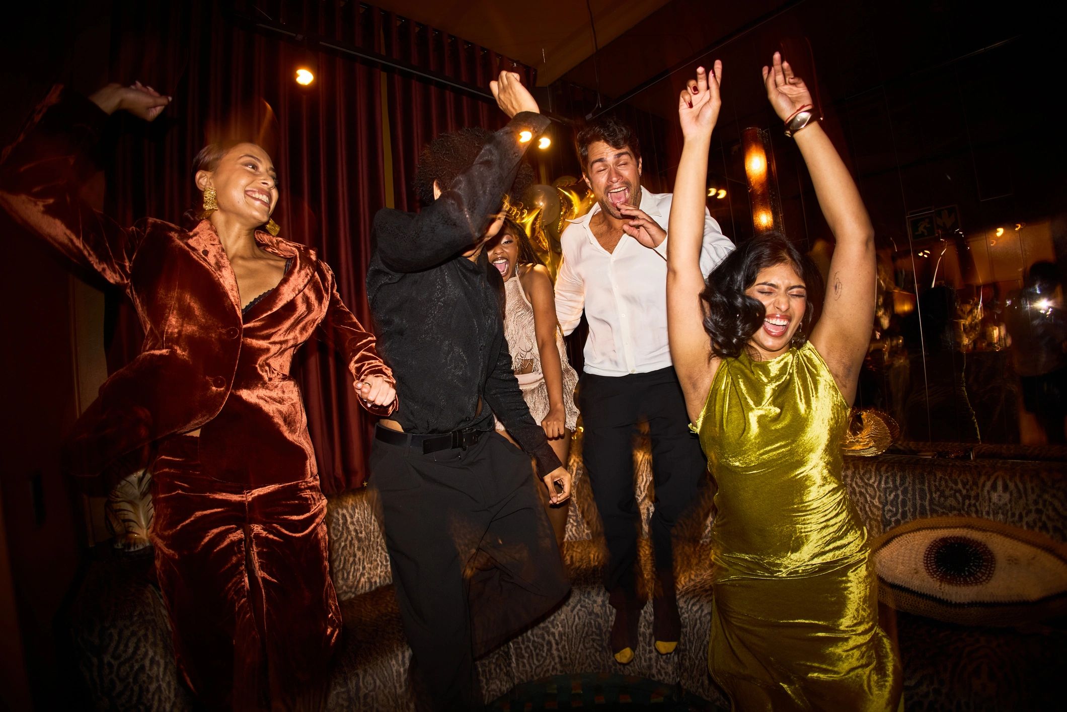 Group of joyful young friends cheering with raised arms on the dance floor during a lively New Year’s Eve celebration